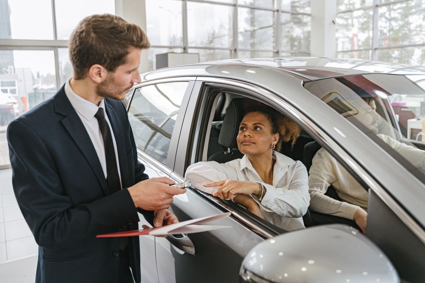 Car dealer handing keys to a buyer sitting in a vehicle